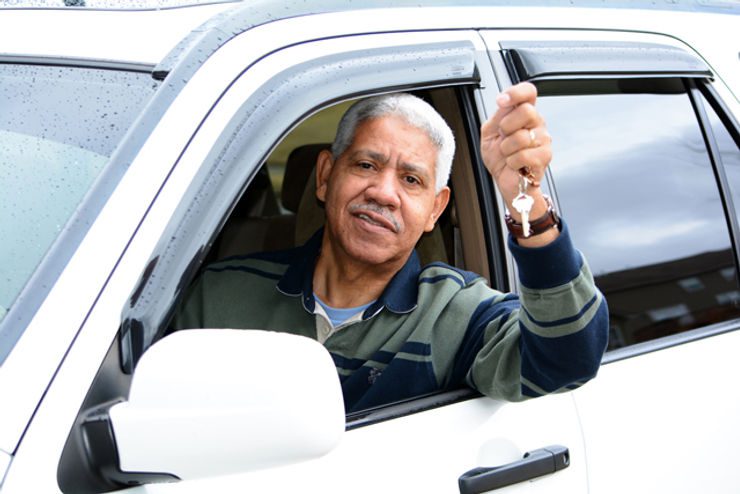 Man driving car, holding up key.